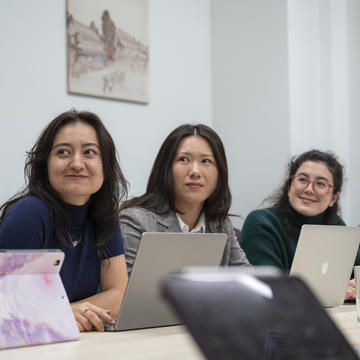 Three students sitting side by side at a table, with laptops open in front of them