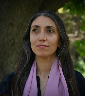 Dr Alice Gaya has long dark hair and is wearing a lilac scarf over a dark blouse. 