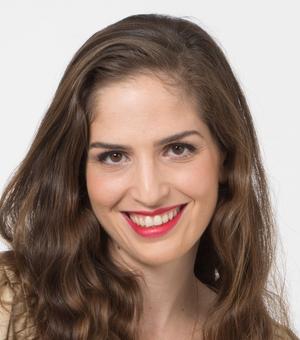 Dr Alfi-Nissan has long brown hair and brown eyes. She is smiling broadly at the camera.