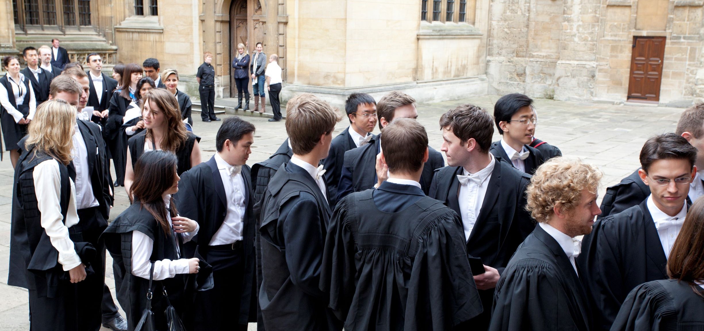 Large group of students in academic dress outside university building 