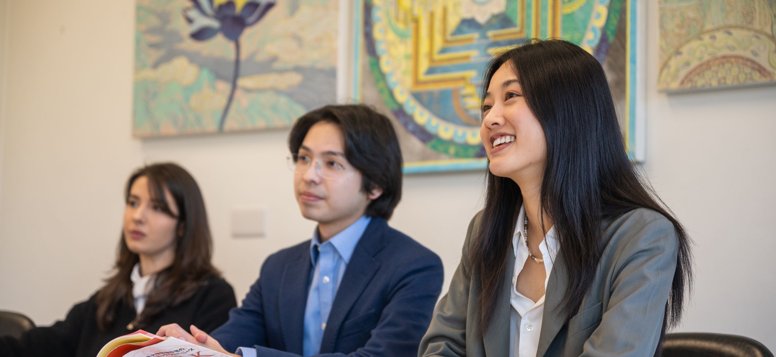 Three students in a seminar with colourful artwork in the background