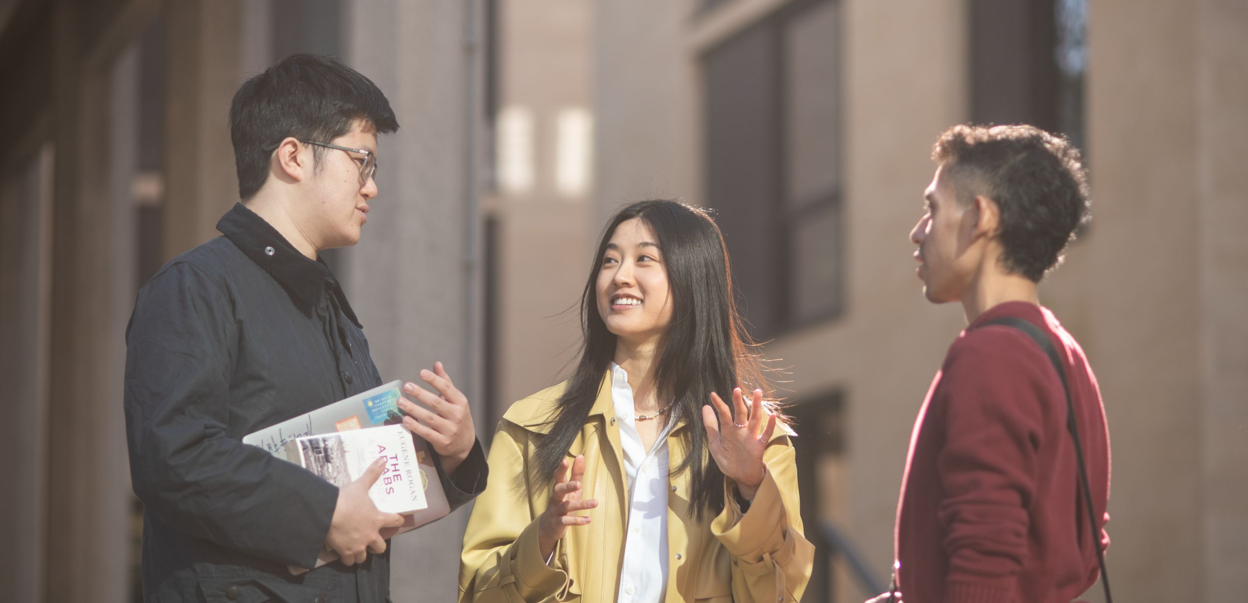 Three students standing outside college building talking