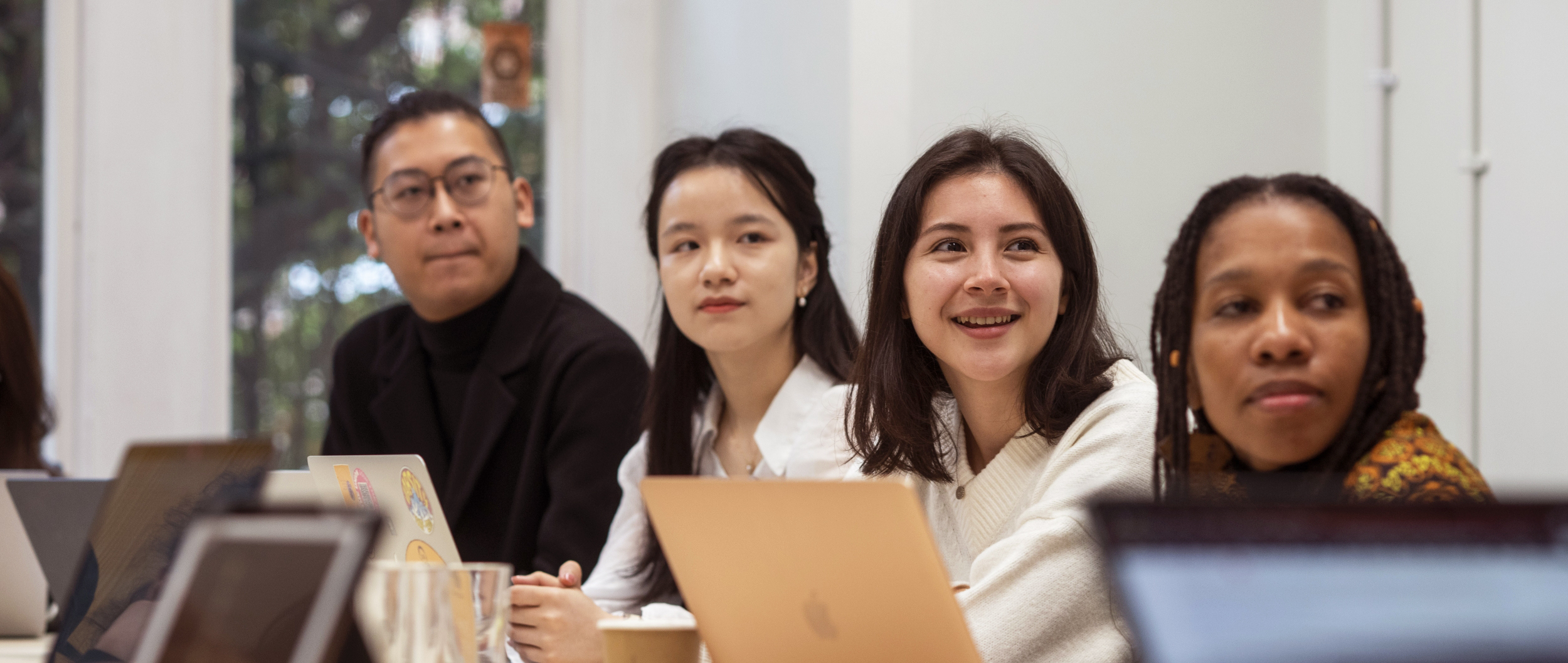 A group of students in a seminar, sat at a table with laptops
