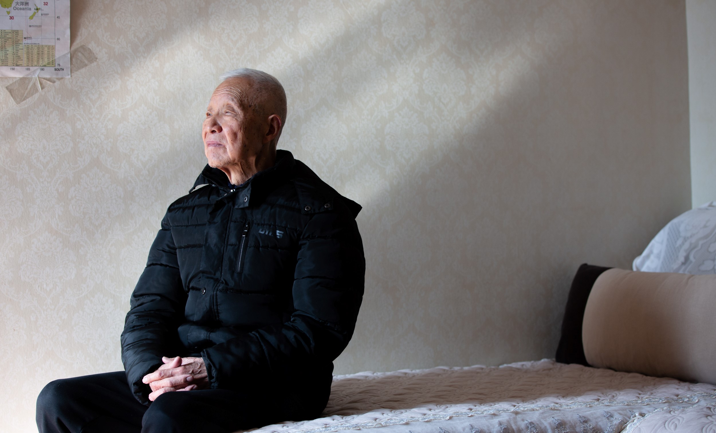 Image of an elderly man sitting at the edge of a couch, looking outwards.