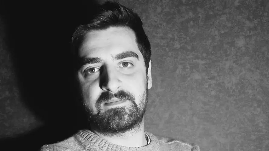 A black and white photo of Giorgi Cheishvili, who has short dark hair and is standing with his arms folded