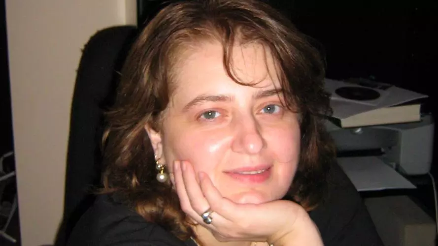Nino Kavtaria has short brunette hair. She is wearing black top and leaning forward, resting her chin on her hand