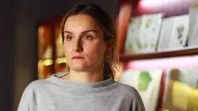 Dr Batiashvili is wearing a grey jumper and standing in front of a display cabinet, looking to the left of the camera