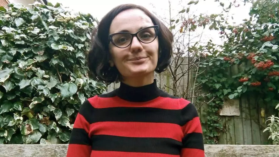 Salome Tsopurashvili has short dark hair and glasses. She is wearing a red and black striped top and is sat on a bench