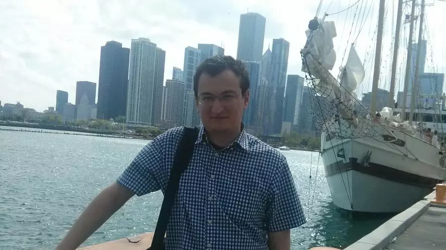Shota Matitashvili is standing on a boat, leaning against the handrail with a city skyline in the background