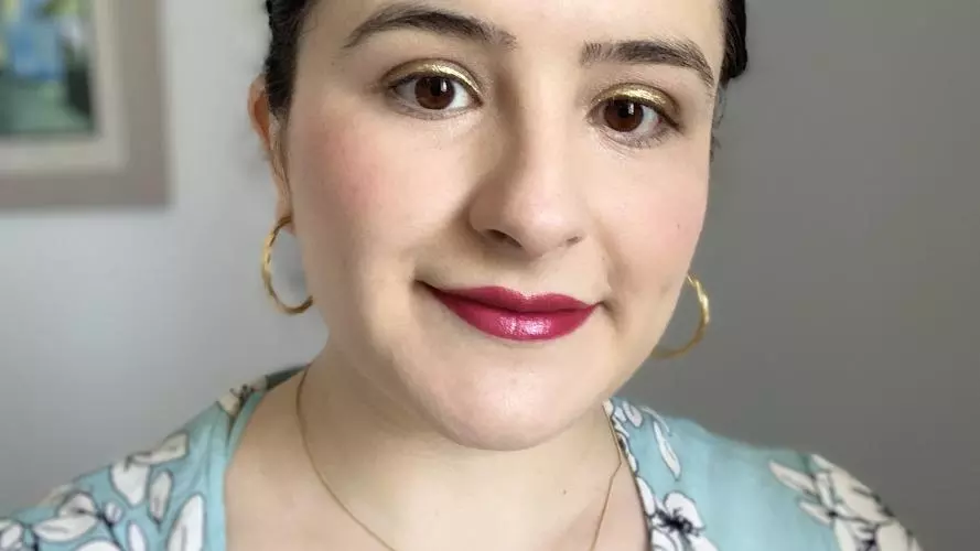 Loreno has her dark hair swept back from her face, and wearing gold hoop earrings. Her top is powder blue with white flower pattern.