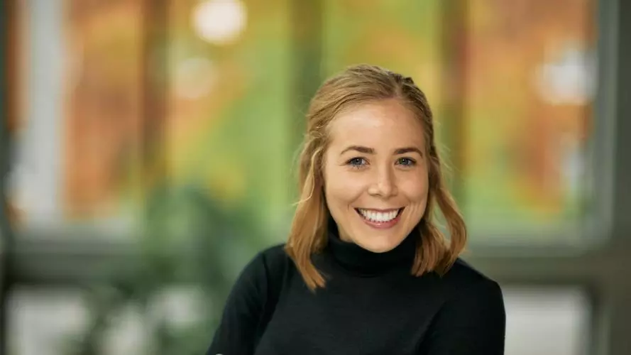 Dr Marnie Howlett has shoulder length blonde hair and is smiling broadly at the camera. She's wearing a black polo neck sweater. She has her arms folded in front of her.  