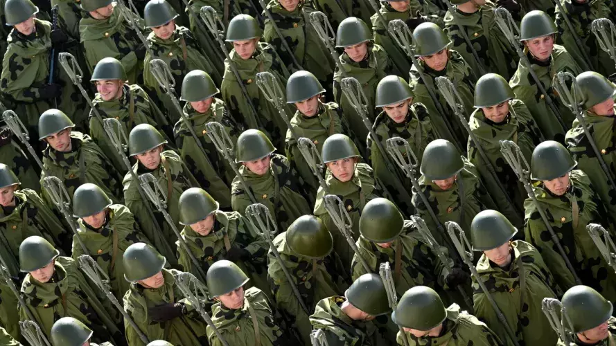 An overhead shot of rows of around 30 soldiers in green camouflage uniforms, helmets and carrying equipment. 