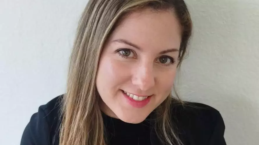 Dr Villegas Plá has long blonde hair. She is wearing a black top and blazer, looking upwards slightly at the camera and smiling. 