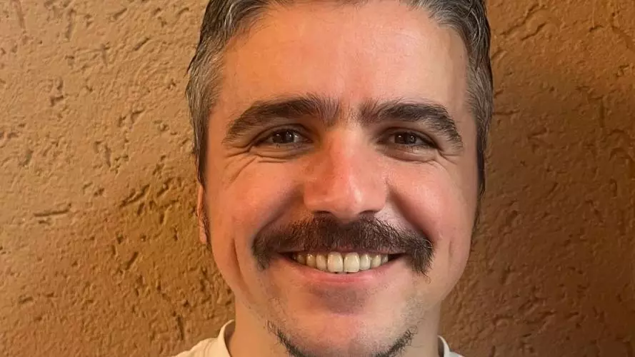 Dr Belder has short dark hair and is wearing a white t-shirt. He is smiling at the camera.