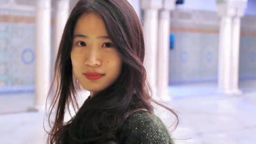 Dr Liu is standing side on, looking at the camera. She has long dark hair and is wearing an oversized dark green knitted cardigan.