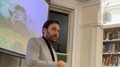 Gregory Thaler standing at the front of a room, presenting in front of a screen