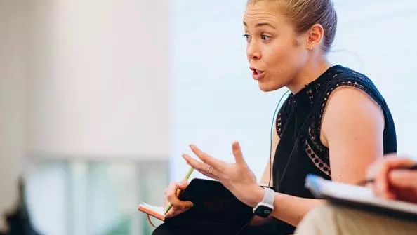 dr marnie howlett has blonde hair worn in a bun. She's wearing a black short sleaved dress and is talking whilst gesturing with her hands. 