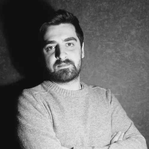 A black and white photo of Giorgi Cheishvili, who has short dark hair and is standing with his arms folded