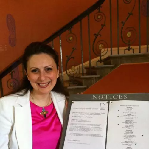 Dr Giviashvili is wearing a bright pink top and white blazer. She is standing next to a board of notices