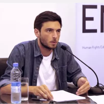 Dr Eristavi has short dark hair and is wearing a denim shirt. He is sat at a desk and speaking into a microphone