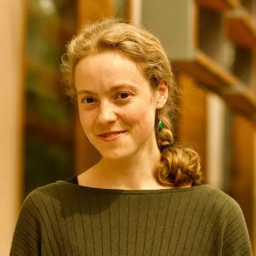 Dr Driessen has curly fair hair tied in a plait. She is wearing a green sweater