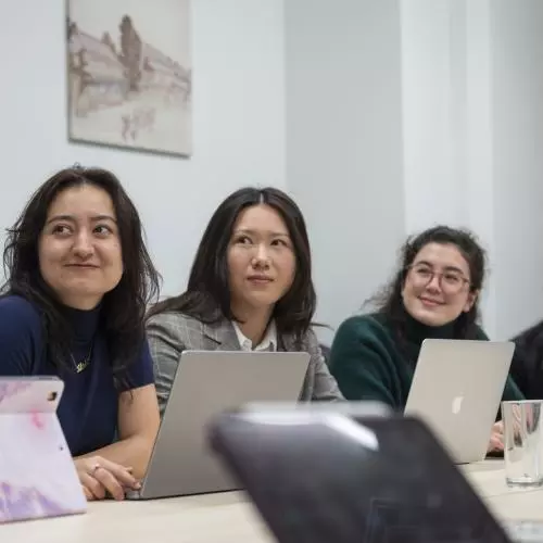 Three students sitting side by side at a table, with laptops open in front of them