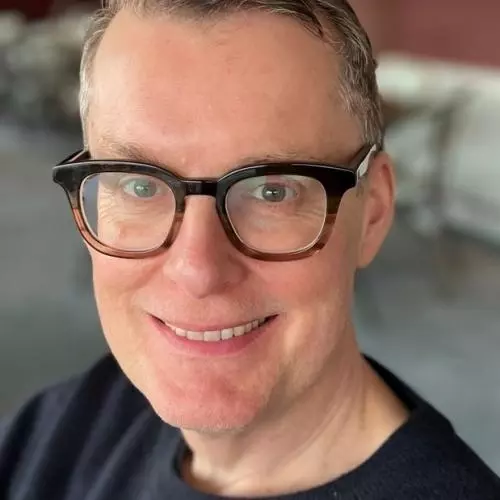 Professor paul chaisty has short dark grey hair, glasses and is smiling at the camera. He's wearing a black t shirt. 