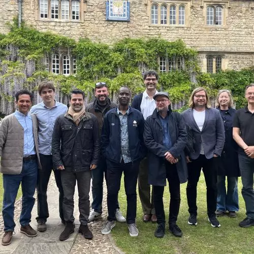 Felip Krause has dark hair, grey beard and is wearing a jacket and black jeans. He's standing with a group of ten people in a college garden.