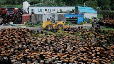 A yard showing single storey buildings, a yellow digger and a field covered with asphalt materials
