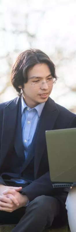 Two students sitting on a bench outside, looking together at a laptop that one of them is holding on her lap. 