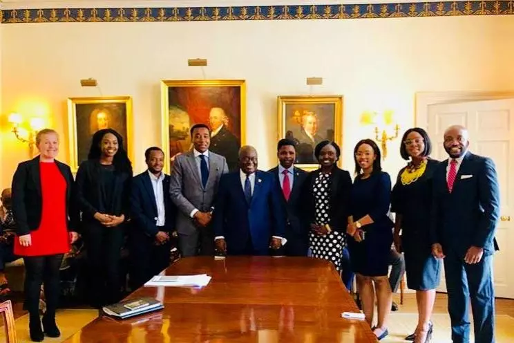 ghanas president and other people in suits standing alongside a large wooden table. Everyone is smiling at the camera. 