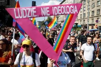 A crowd of people walking down a street holding rainbow flags and a pink triangle with the text 'LUDZIE, NIE IDEOLOGIA'. 